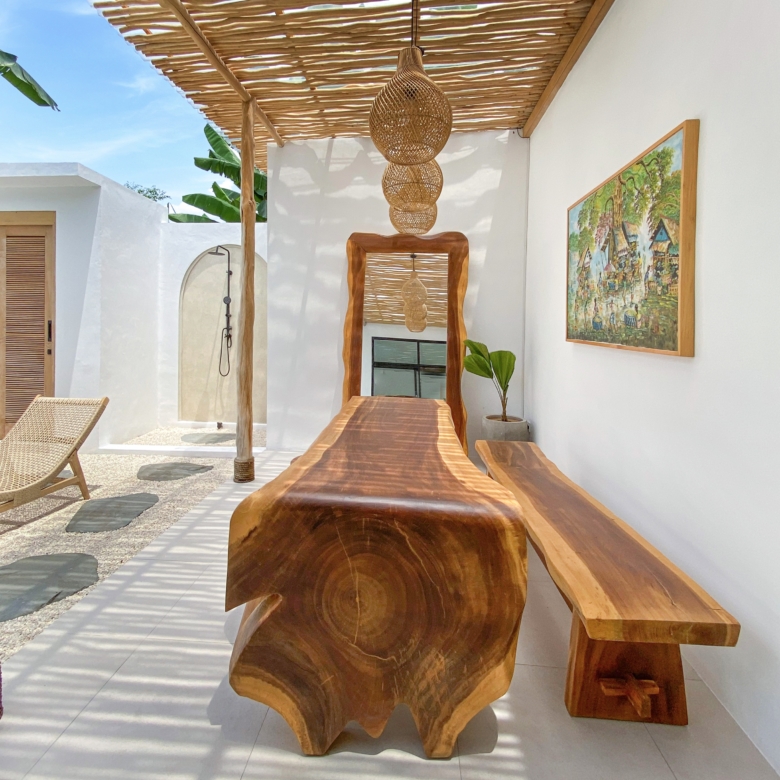 Handcrafted live-edge wooden table and benches under a bamboo pergola with woven rattan pendant lights in a bright outdoor patio.