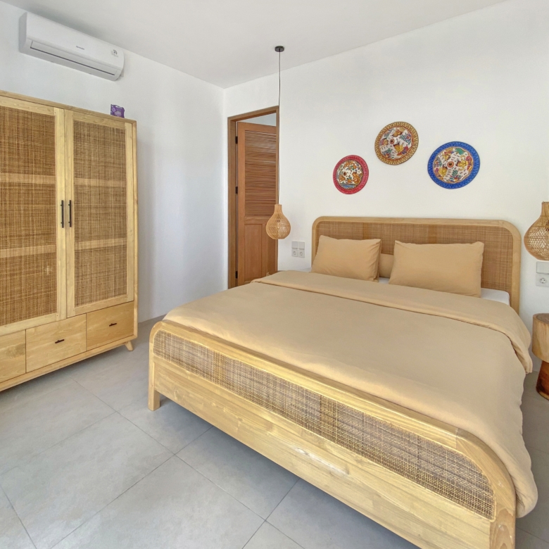Bedroom with beige bedding, wicker headboard, and light wood wardrobe; two pendant lamps and decorative plates on the wall.