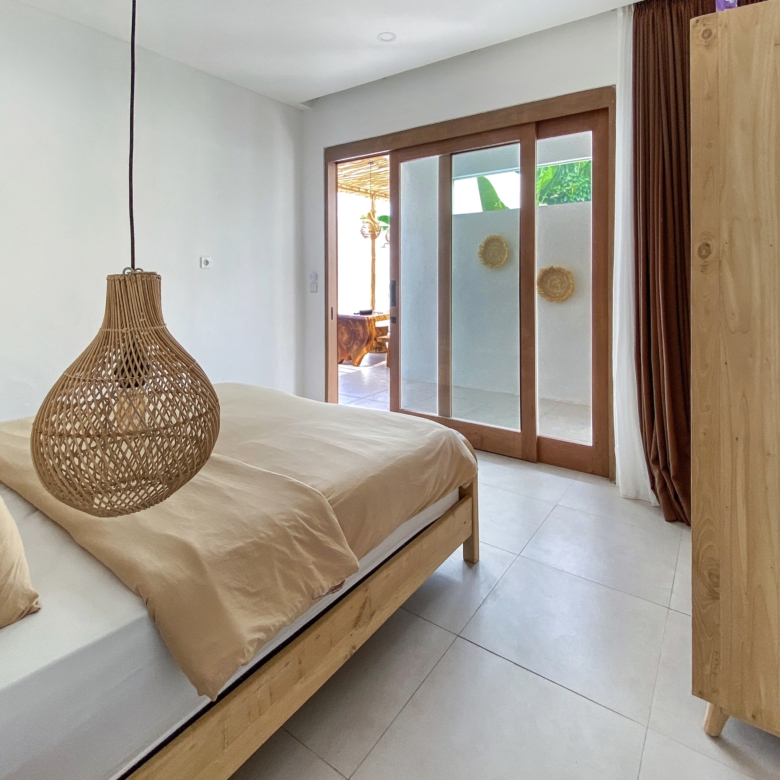 Twin beds with beige bedding and wicker pendant lights in a sunlit wood-furnished bedroom.