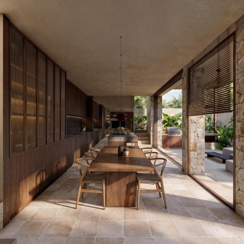Open-plan outdoor dining area with a long wooden table and chairs, kitchen wall on the left, overlooking a pool and tropical garden.