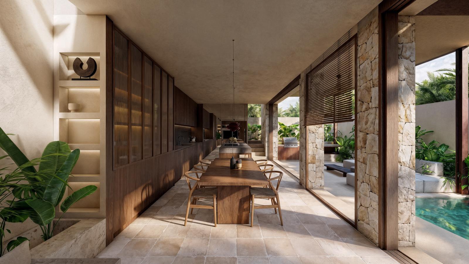 Open-plan outdoor dining area with a long wooden table and chairs, kitchen wall on the left, overlooking a pool and tropical garden.