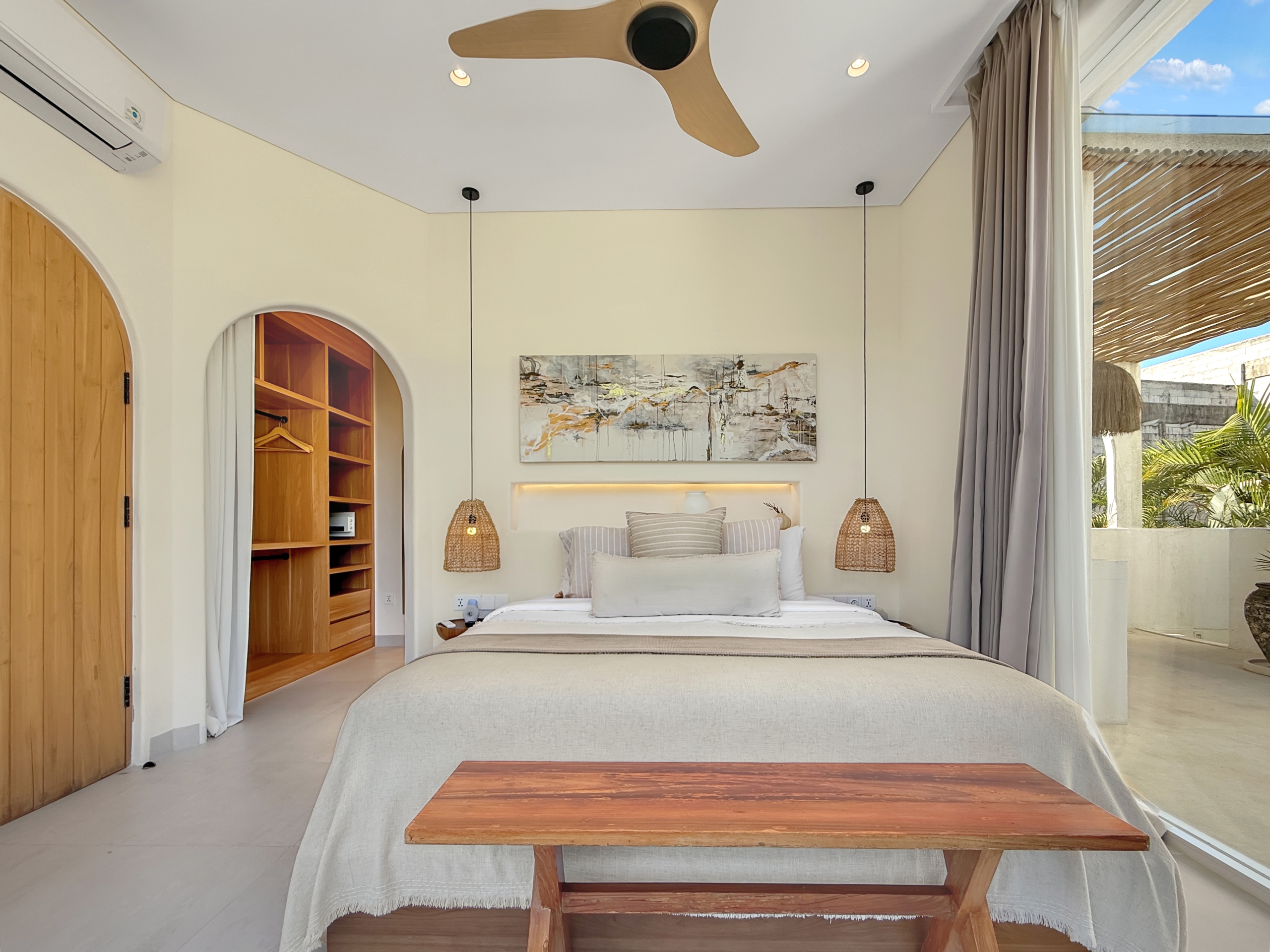 a14c2e1fdd679bd1ca3ed39bea6165142aad28d9 Bright bedroom interior with a large bed, two woven pendant lamps, and a wooden coffee table in the foreground.