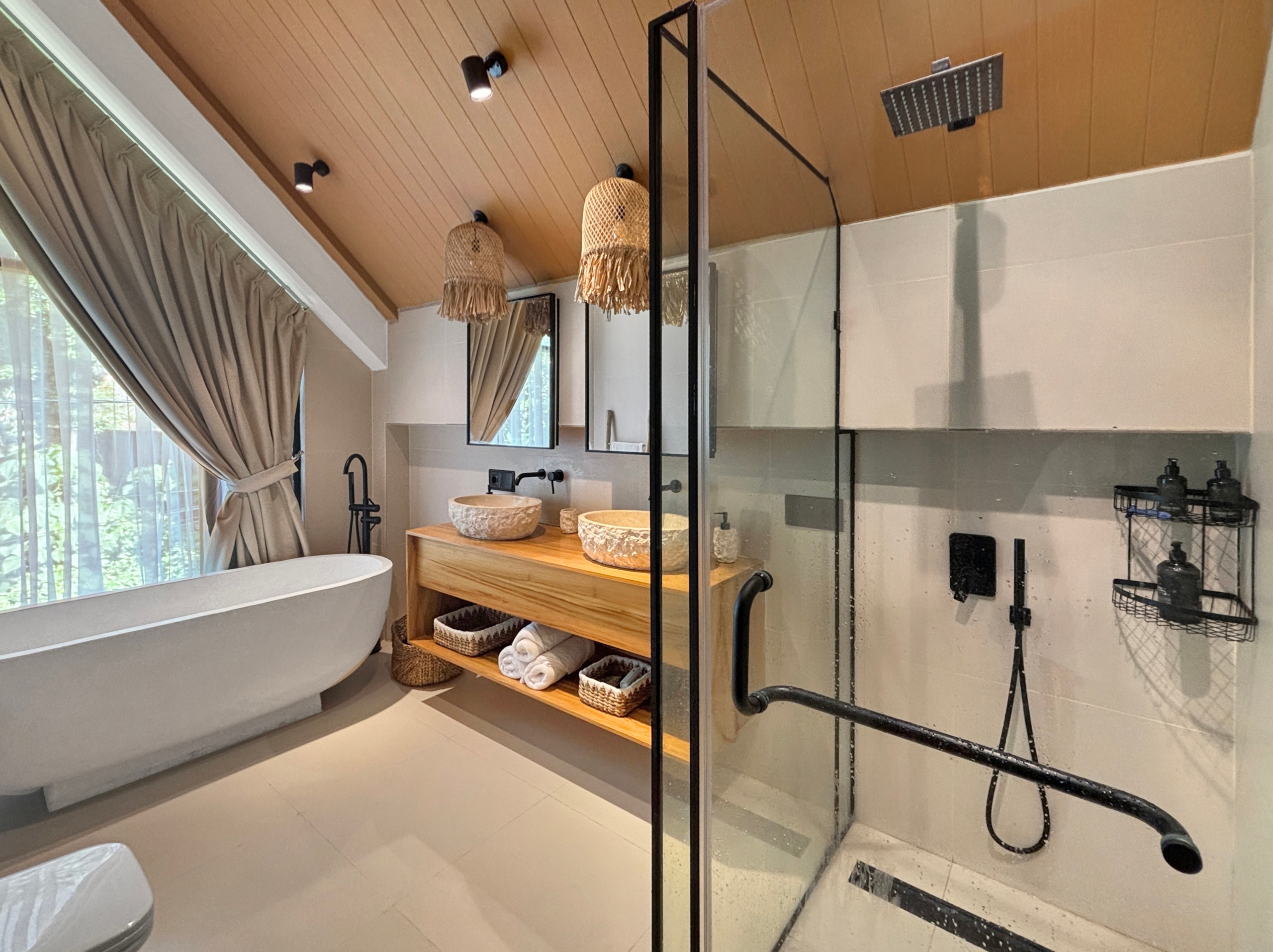 a7eb023794fc48898bfc3619491413969026a65d Spa-like bathroom featuring a freestanding oval tub, wooden vanity, and glass-enclosed shower with black fixtures and woven pendant lights.
