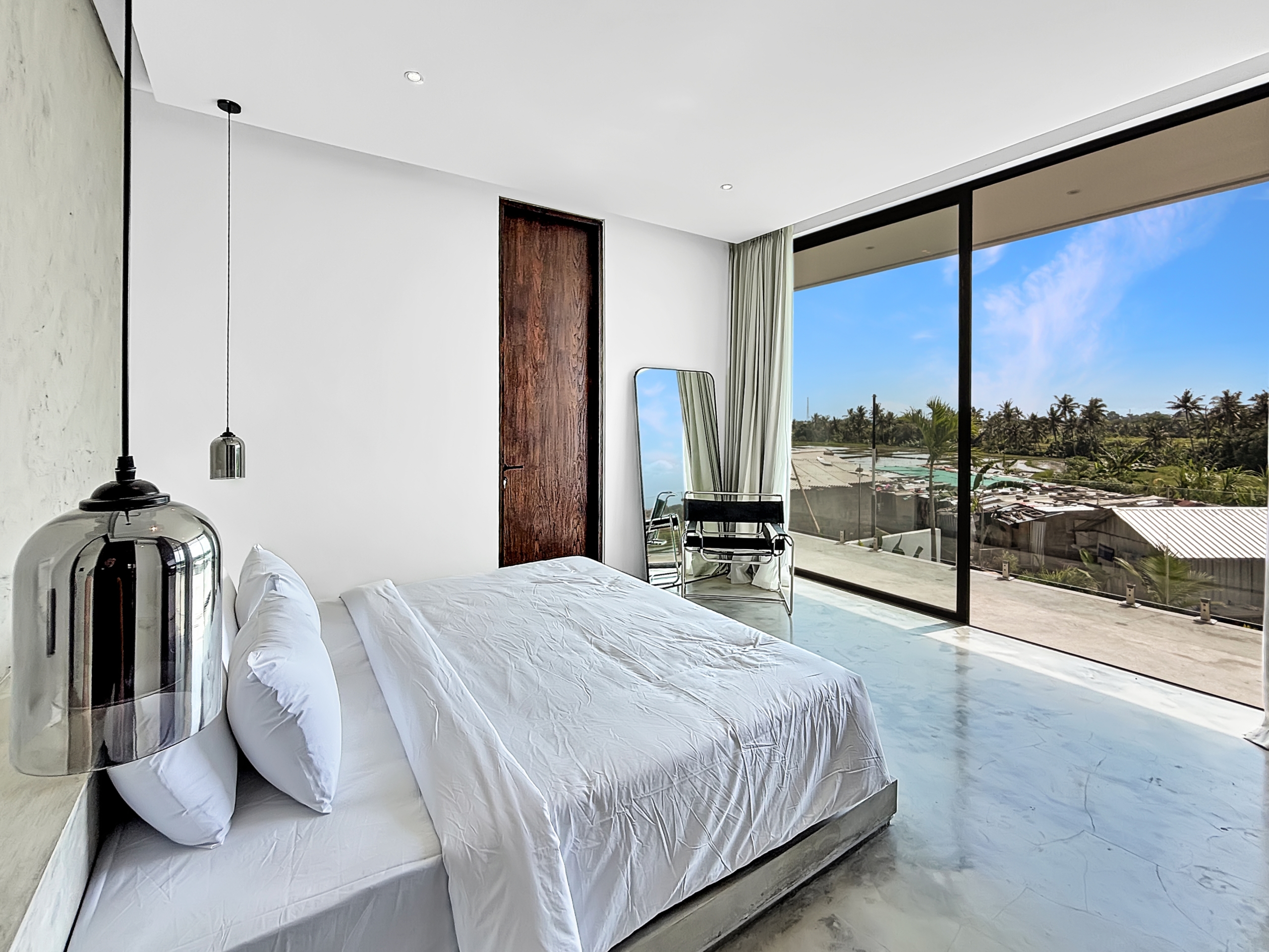 a9e4627620d751edcbcc81989c287cac91f1b84e_6770-6a1d7baed9e59 Bright modern bedroom with white bedding on a low platform bed, Nana glass wall showing palm trees and a blue sky outside.