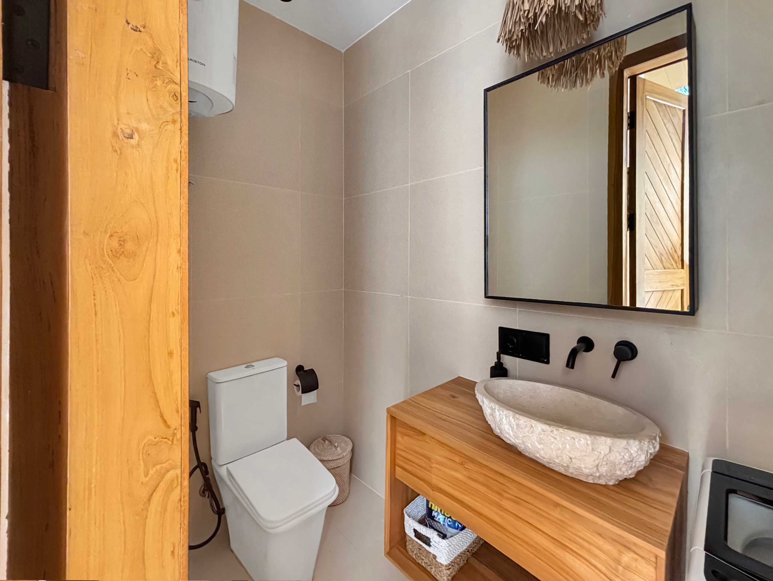 ab31cad9af190ca9f06c062aabf3d5cb4e3ce00d Bathroom with a white toilet and vessel sink on a wooden counter, reflected in a large wall mirror. The space has beige tile walls and a wooden door frame adjacent.