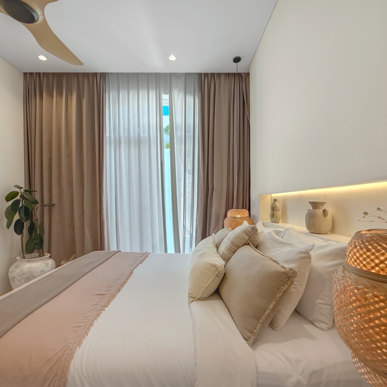 Modern hotel-style bedroom with two neatly made beds in neutral tones, beige pillows, brown curtains, and a potted plant in the corner.