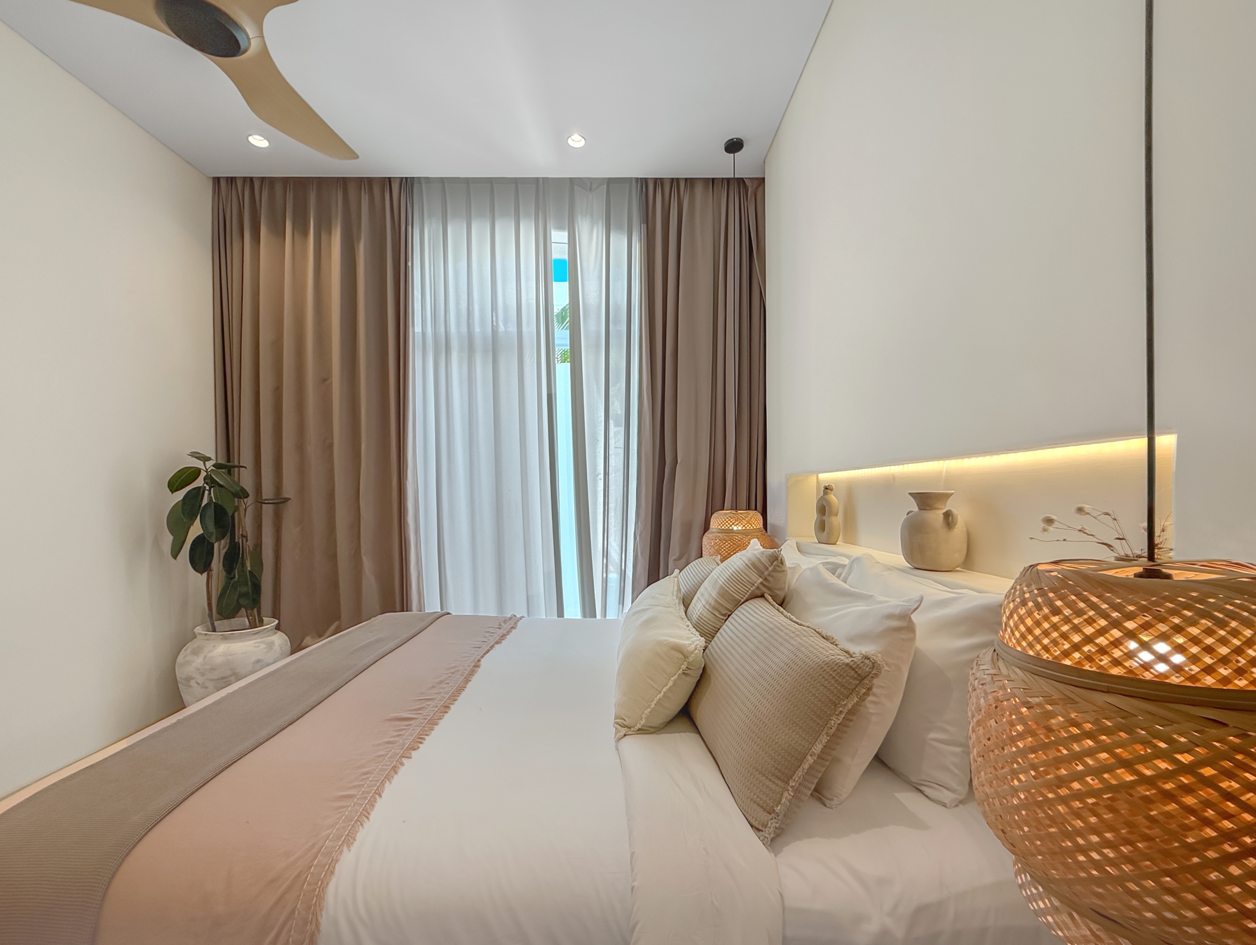 ab52a7d3c3d5e17b81180a969e6bb58c8601bf04 Modern hotel-style bedroom with two neatly made beds in neutral tones, beige pillows, brown curtains, and a potted plant in the corner.