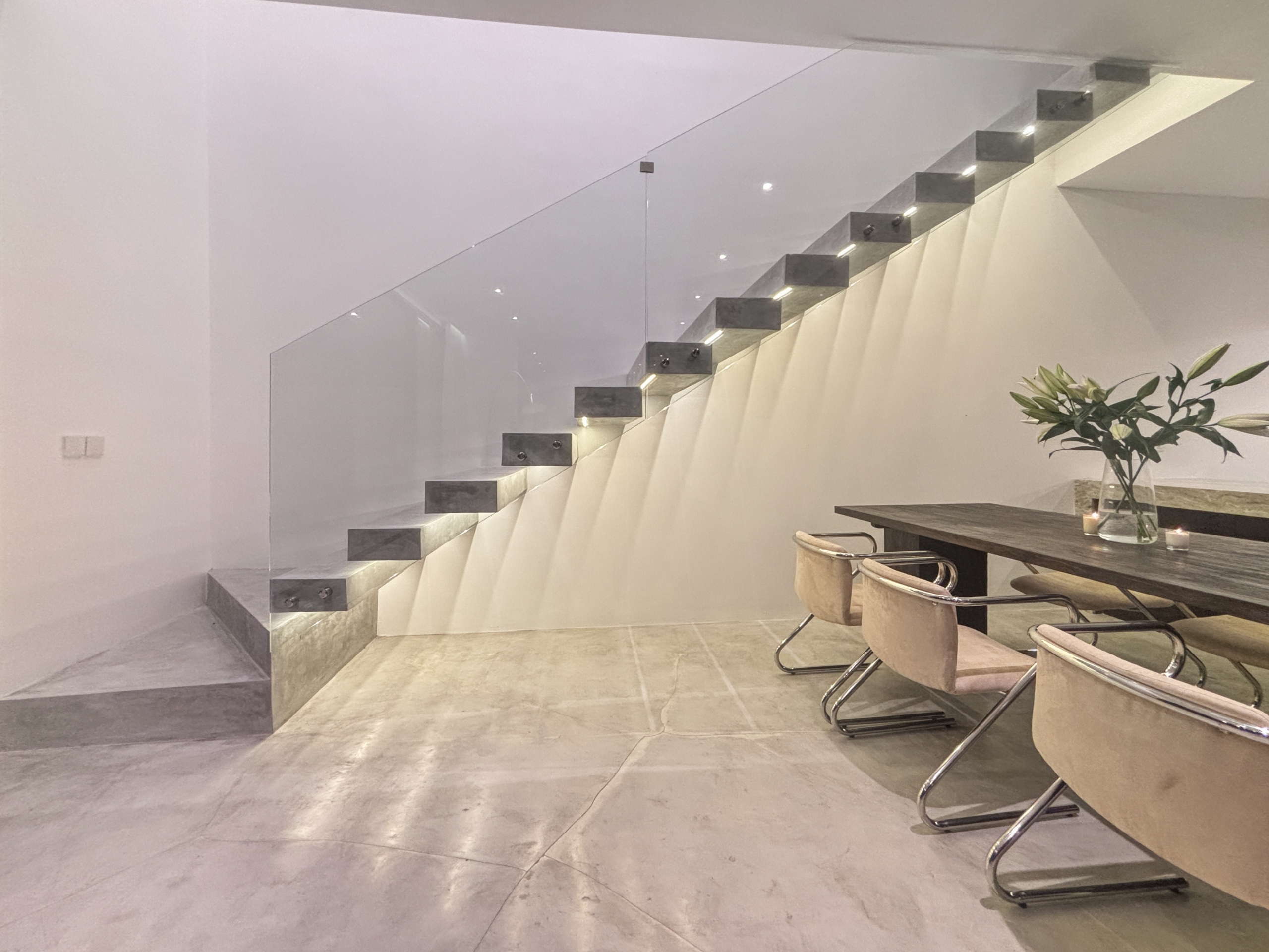 ad5a722d64549dfc4e029c71170e524187529434_0957-6a05be0729f21 Modern interior with a glass-railed, floating staircase beside a dining table and beige chairs.