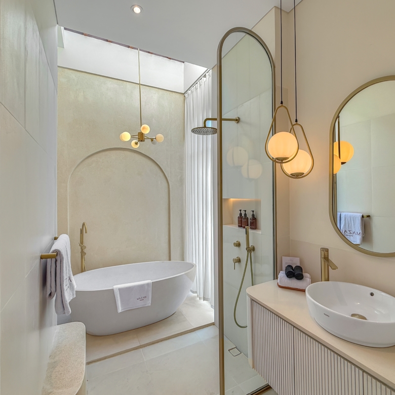 Luxurious bathroom with a white freestanding oval tub, glass shower, and gold fixtures beneath arched mirrors.