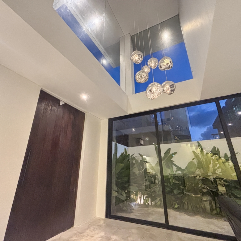 Interior corner with hanging glass globe pendant lights and large floor-to-ceiling windows showing greenery outside, in a modern lobby.