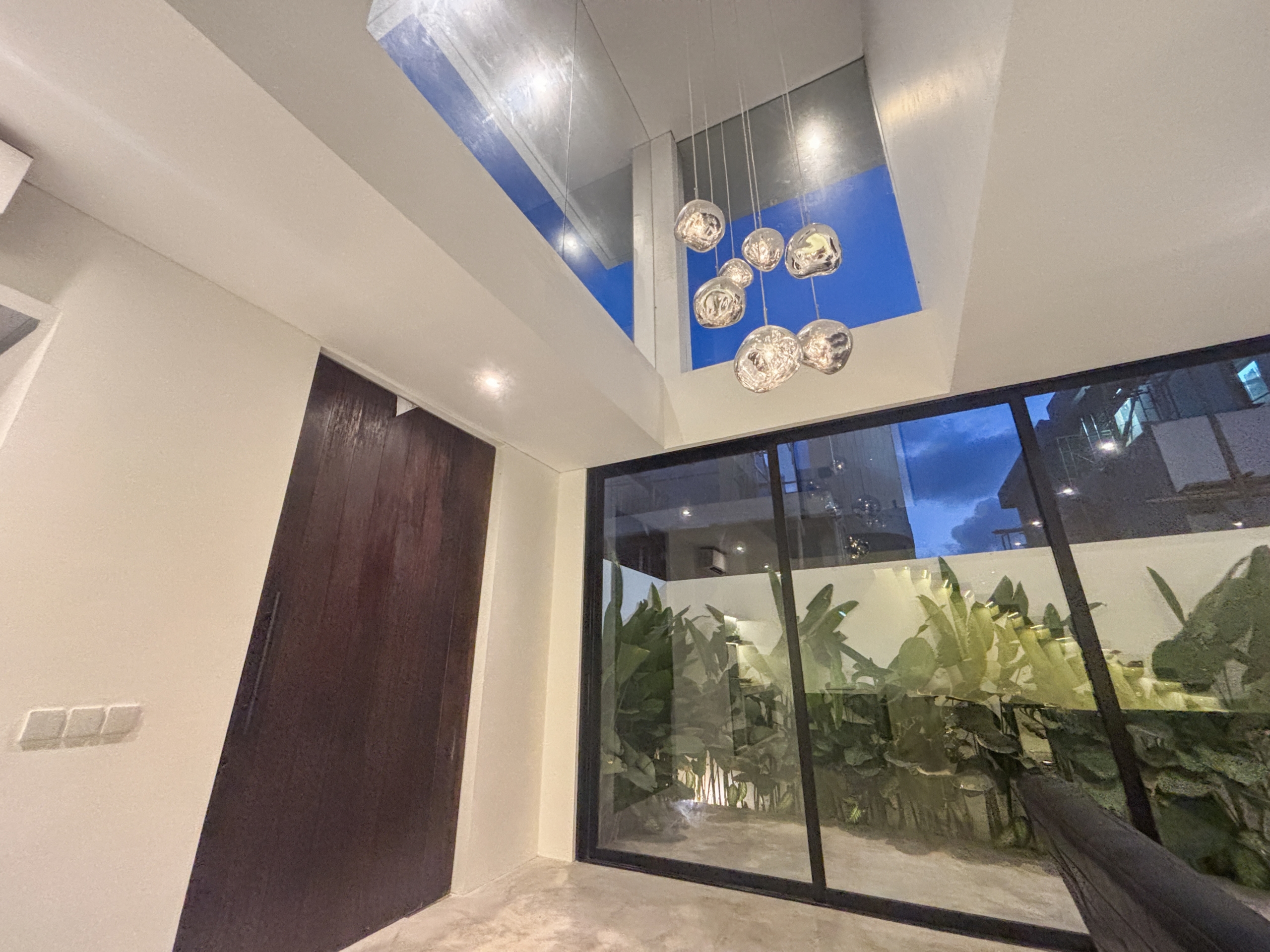b5cdc28c4ebabd6214d9e318d9413d6613cb505e_0976-6a05be04e16fa Interior corner with hanging glass globe pendant lights and large floor-to-ceiling windows showing greenery outside, in a modern lobby.