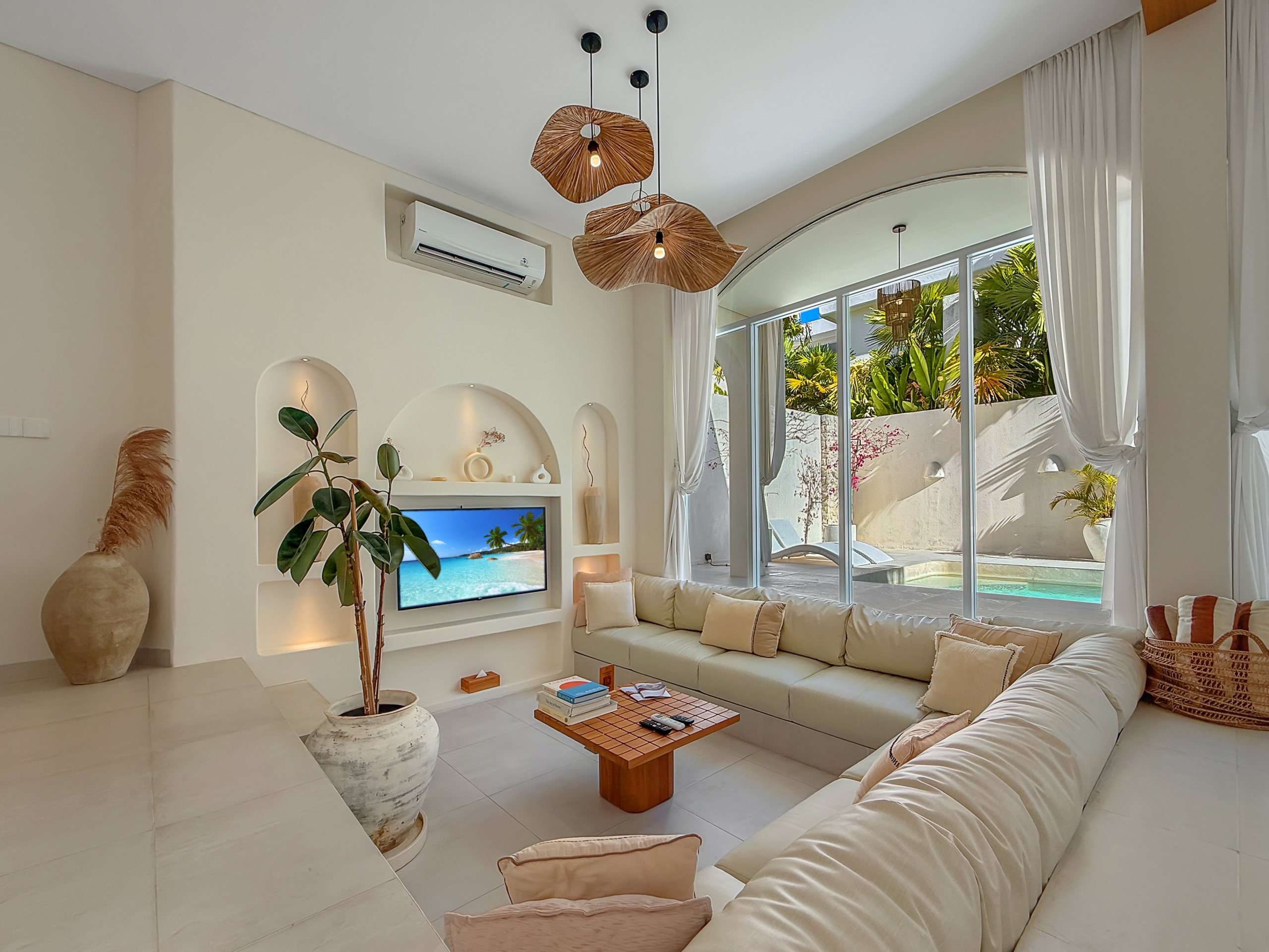 b7b1393443e698e1463cd93f3413af64452a8959 Bright living room with a white sectional sofa, hanging woven pendant lights, and large glass doors showing a pool and palm trees outside.