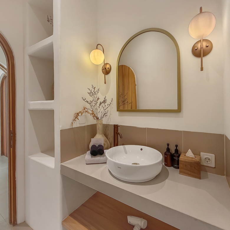 Round vessel sink on a raised countertop with a brass-framed arch mirror and warm wall sconces in a modern bathroom vanity area.