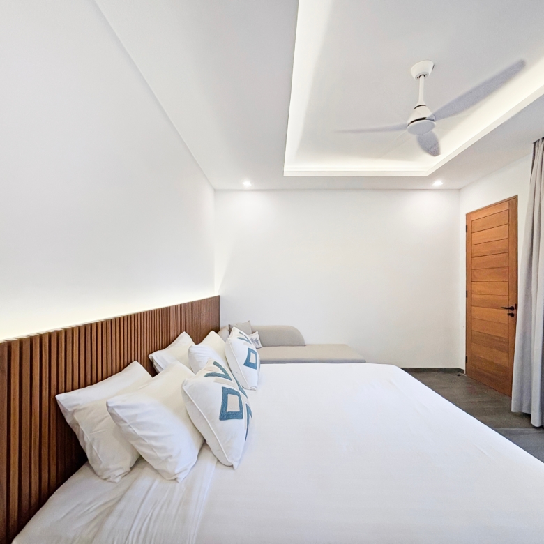 Hotel room with two white beds and a wooden slatted headboard, light walls, and gray curtains by a wooden door.