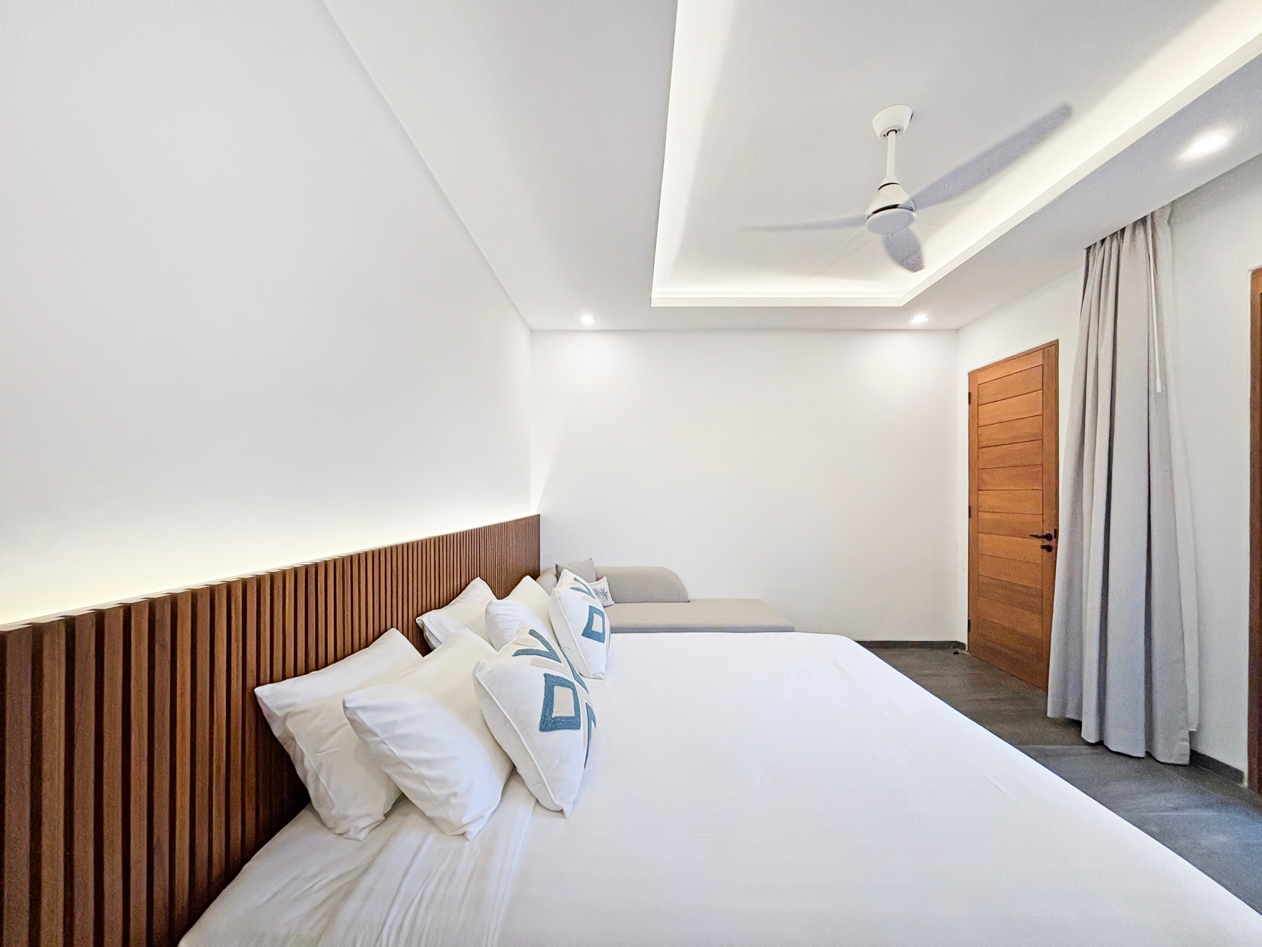 ba48d742e129fe386eed3abb2db43c3ae5a8dccf Hotel room with two white beds and a wooden slatted headboard, light walls, and gray curtains by a wooden door.