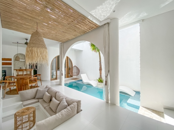 Bright open living area with a large woven pendant lamp, white walls, and a turquoise pool visible through arches.