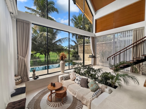 Bright, airy living room with floor-to-ceiling glass walls showing palm trees and a pool outside; neutral seating and woven rug.