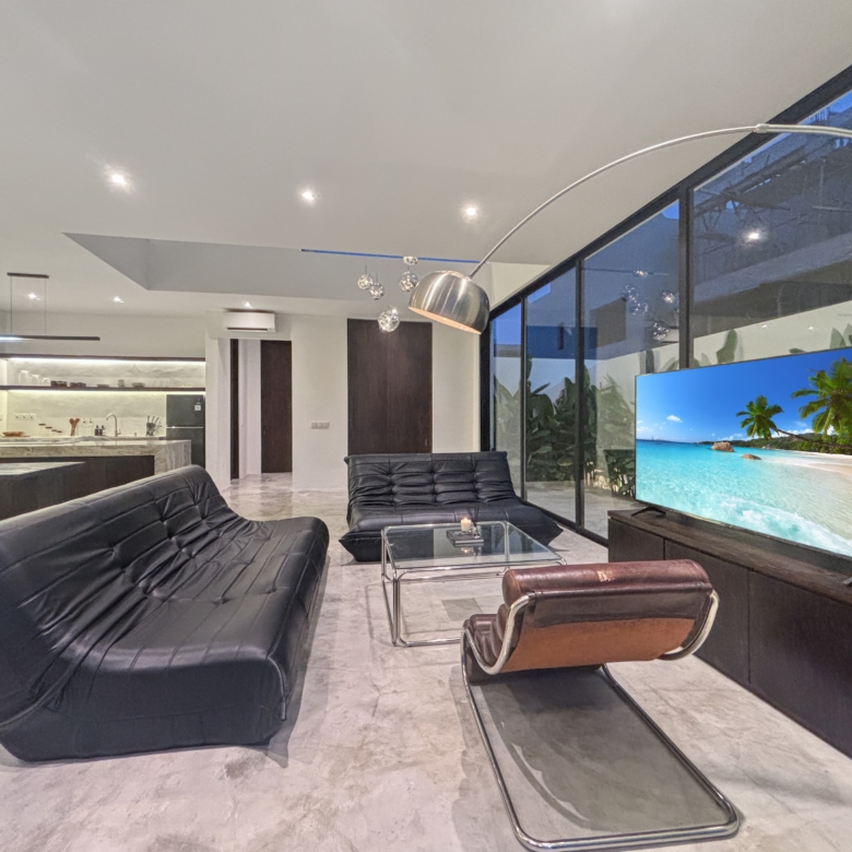 Contemporary living room with black leather lounge chairs facing a large flat-screen TV displaying a tropical beach scene.