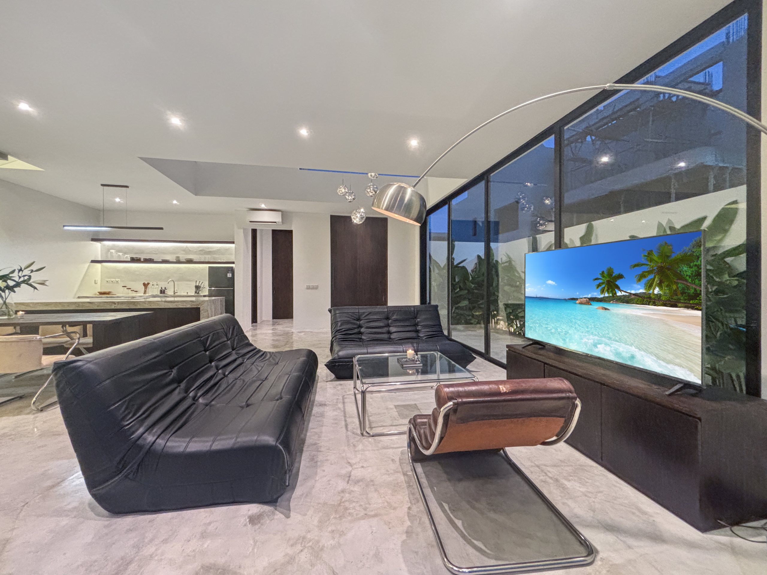 d3bedf2127954642ac1e4e6ad264812448f19696_0991-6a05be054fc22 Contemporary living room with black leather lounge chairs facing a large flat-screen TV displaying a tropical beach scene.