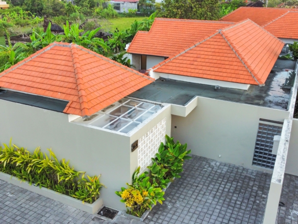 Aerial view of a modern house with orange terracotta roof tiles and a gray paved courtyard surrounded by tropical plants.