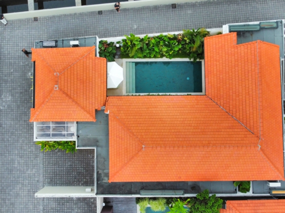 Aerial view of orange-tiled rooftops surrounding a rectangular pool with greenery along the edges and gray tiled walkways nearby.
