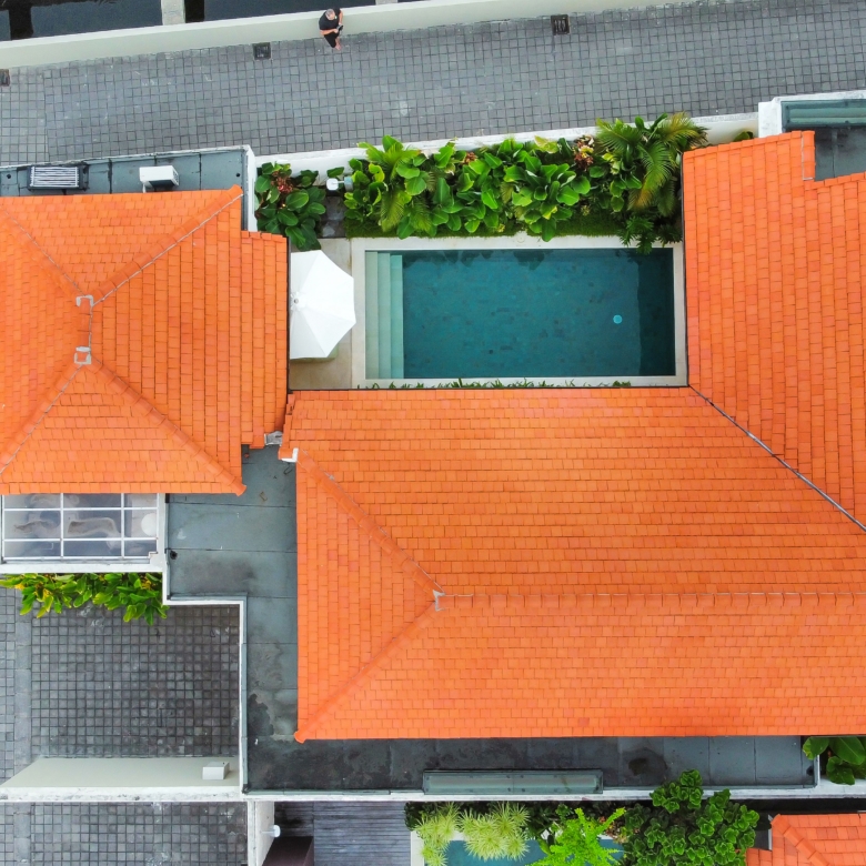 Aerial view of orange-tiled rooftops surrounding a rectangular pool with greenery along the edges and gray tiled walkways nearby.