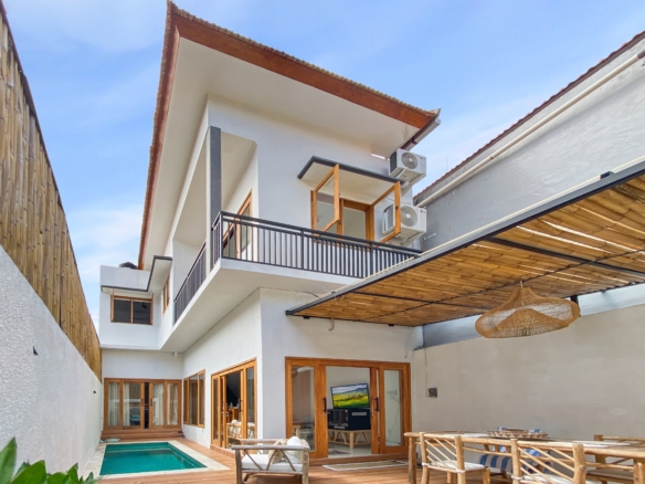 Modern white house with wooden-framed glass doors, a narrow pool, and a shaded outdoor seating area beneath a blue sky.