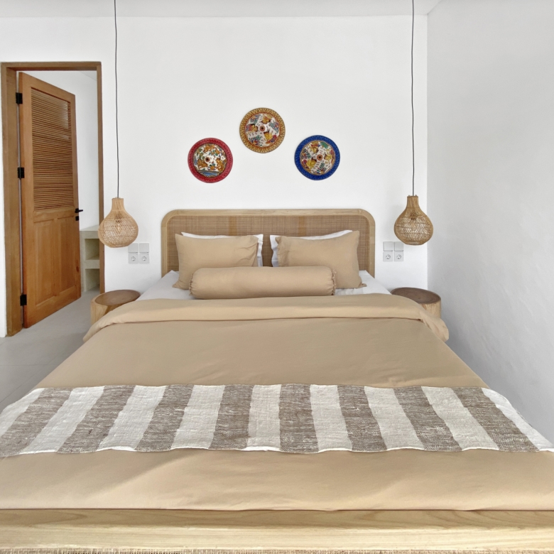 Beige bedroom with a striped bed runner, beige pillows, and a rattan headboard under three colorful circular wall plates.