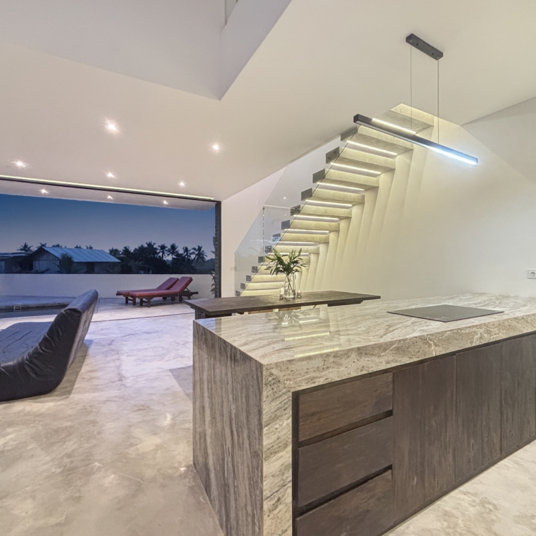 Open-plan interior with a marble kitchen island, dark wood cabinetry, and a floating glass-railed staircase along the wall.