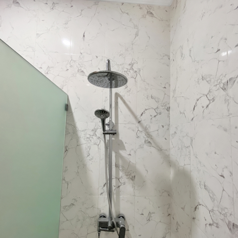 Modern bathroom shower with a large round rain head and handheld wand on a marble-tiled wall enclosure, chrome fixtures visible.