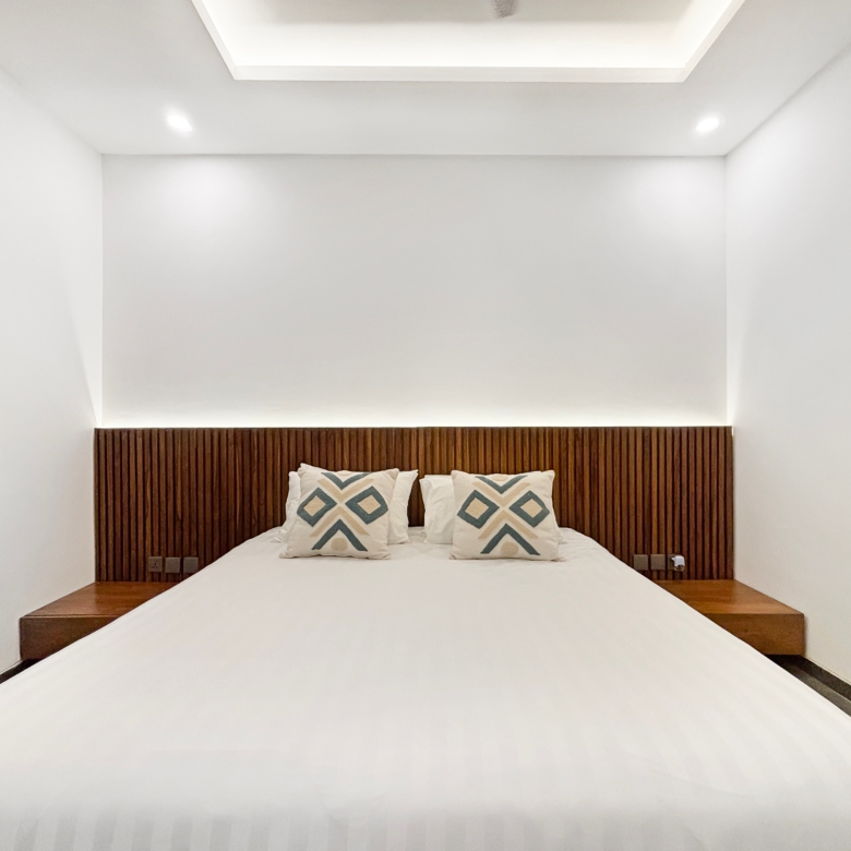 Minimalist bedroom with white bedding and a dark wooden, vertically slatted headboard behind the bed.
