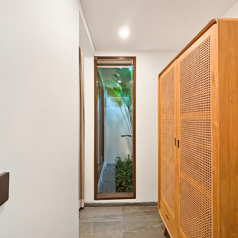 Narrow indoor hallway with white walls, tile floor, ceiling light, and a tall wooden cabinet with woven cane panels on the right.