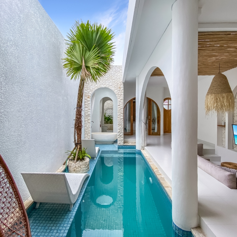 Poolside courtyard with a narrow turquoise pool, white walls, and palm tree under a blue sky.