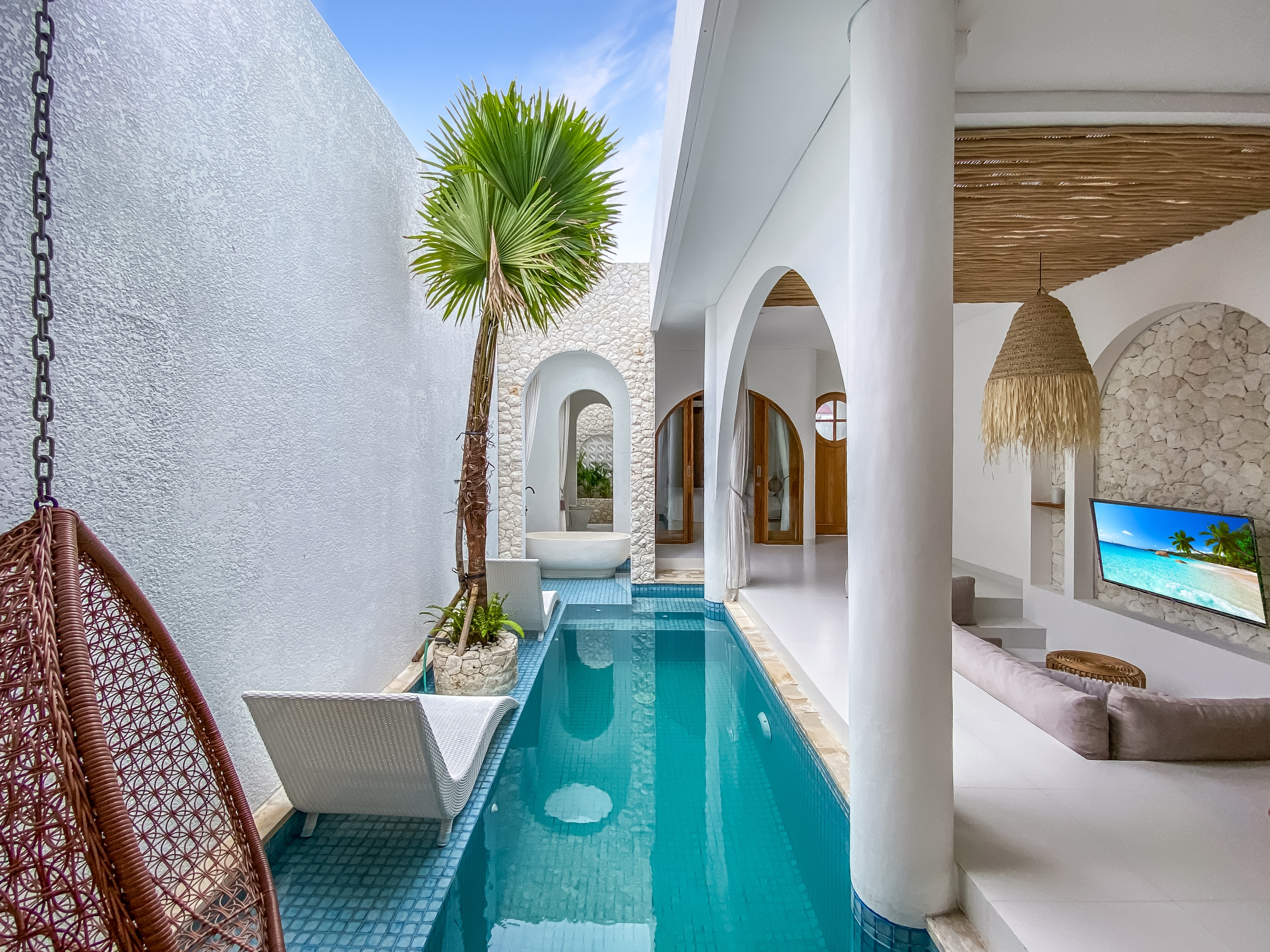f89d6eff08f67071fdd443a232bf866d59ad0f4f Poolside courtyard with a narrow turquoise pool, white walls, and palm tree under a blue sky.