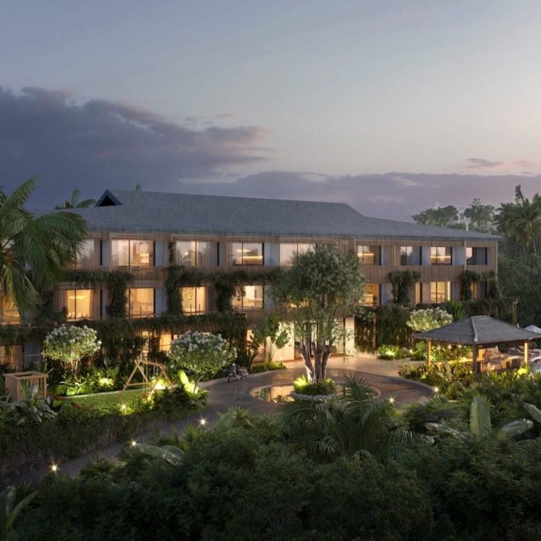 Three-story tropical resort with lit windows surrounded by palms and lush greenery at dusk/twilight.